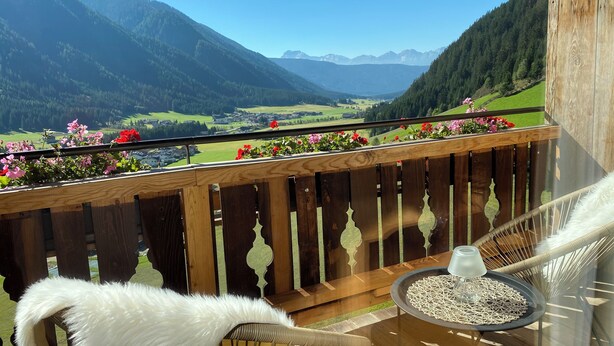 A balcony with a view of a valley and mountains, a wooden railing, a white chair, and a small table with a glass. - Cozy apartment with panoramic views of the Casies Valley (Trentino-Alto Adige)