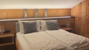 A bedroom with a sloped ceiling, wooden headboard, and three wooden wall decorations. - Cozy apartment with panoramic views of the Casies Valley (Trentino-Alto Adige)