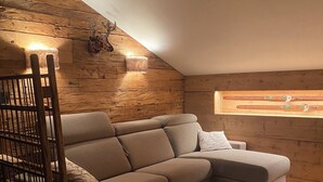 A cozy loft bedroom with a large L-shaped sectional sofa, a wooden ladder, and a rustic wooden wall. - Cozy apartment with panoramic views of the Casies Valley (Trentino-Alto Adige)