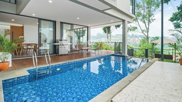 A modern indoor swimming pool with clear glass walls, wooden deck, and a view of greenery. - Sorte by Kozystay - Dago (Cimenyan)