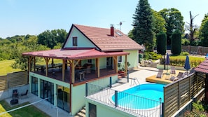 A two-story house with a swimming pool, a covered patio, and a fenced garden area.