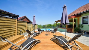 A wooden deck with lounge chairs and umbrellas, a swimming pool, and a view of the landscape.