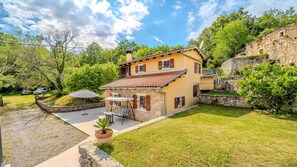 Una casa de dos pisos con un patio, muros de piedra y un césped verde exuberante.