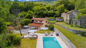 Una villa con piscina, mobiliario exterior y un muro de piedra.