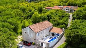 A stone building with a swimming pool, surrounded by dense green trees.