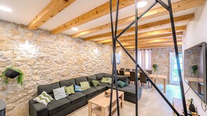 Un salon moderne avec un mur en pierre, des poutres en bois, un canapé d’angle et un coin repas.