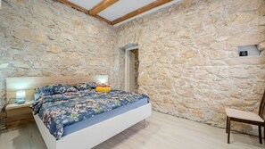 A bedroom with a stone wall, a bed with floral bedding, a bedside table with a lamp, and a chair. - Villa Elefant by Villas Guide (Tribalj)