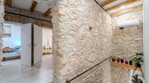 A stone wall interior with a wooden beam ceiling, a bed with colorful bedding, and a shelf with candles and a plant. - Villa Elefant by Villas Guide (Tribalj)