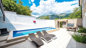 A swimming pool with lounge chairs, a stone wall, and a view of mountains.
