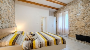 A bedroom with a stone wall, a bed with striped bedding, a wooden headboard, and a window with curtains.