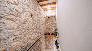 Un étroit couloir en pierre, avec un plafond en bois et un mur blanc d’un côté.