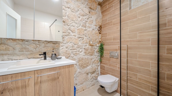 A bathroom with a stone wall, a wooden vanity, a toilet, and a shower area.