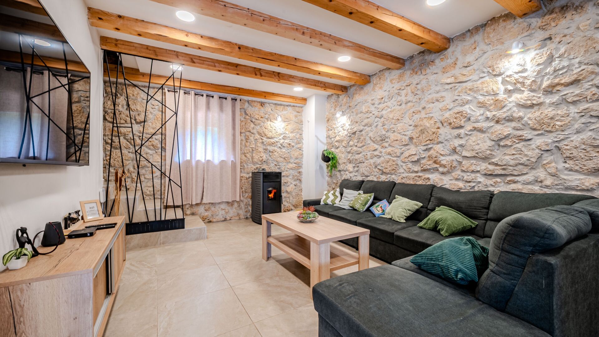 Una sala de estar acogedora con una pared de piedra, vigas de madera, chimenea y un sofá confortable.