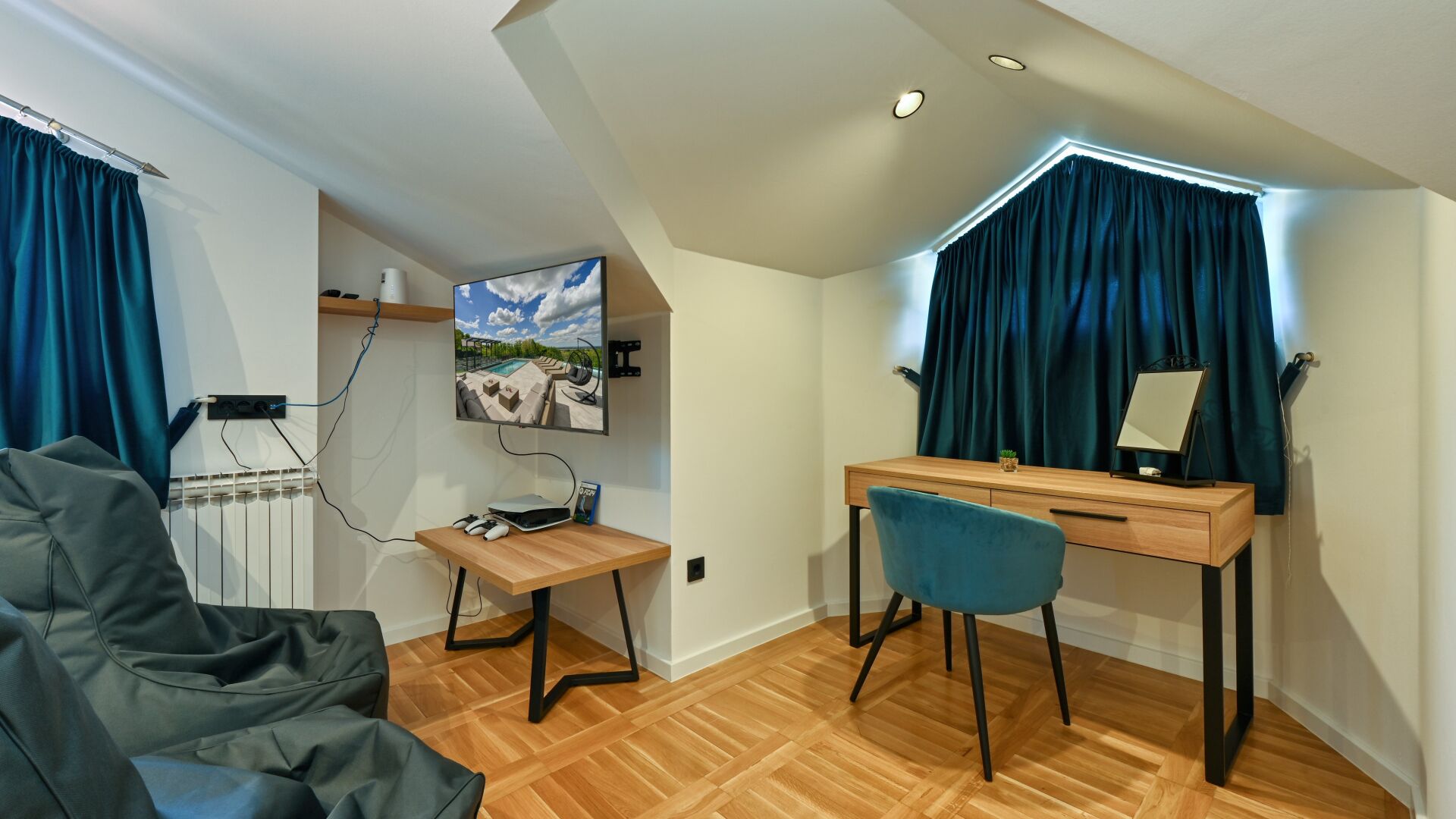 A modern room with a desk, chair, gaming setup, and a large window with curtains.