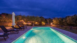 A swimming pool with lounge chairs and umbrellas, surrounded by trees and stone walls.
