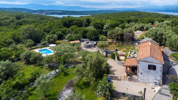 Una villa con piscina, ruinas de piedra y vistas del bosque y las montañas circundantes.
