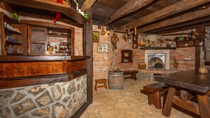 Un interior rústico con pared de piedra, vigas de madera, chimenea y diversos utensilios de cocina.