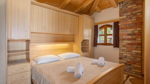 Un dormitorio con cabecera de madera, cama con ropa de cama blanca, ventana con cortinas y pared de ladrillo.