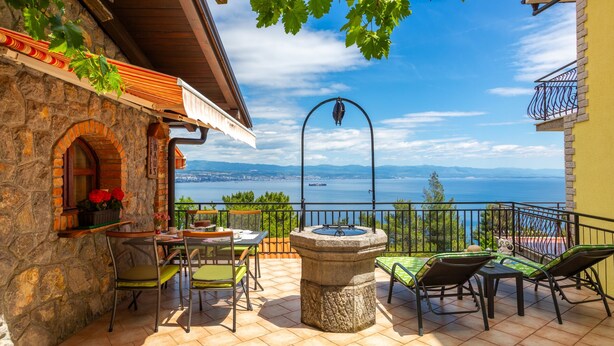 Una terraza con paredes de piedra, una mesa con sillas, una fuente de piedra y vistas al mar.