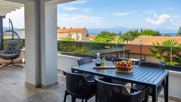 Un balcón con una mesa lista para comer, una silla colgante y vistas al mar y edificios.