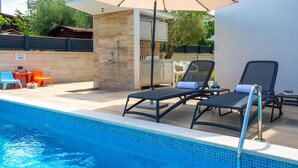 Un área de piscina con sillones, una mesa y un espacio de estar techado.