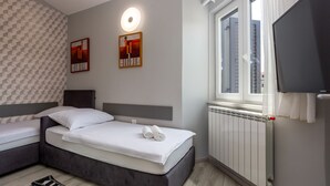 Habitación de hotel con cama, un radiador, una ventana y dos obras de arte colgadas en la pared.