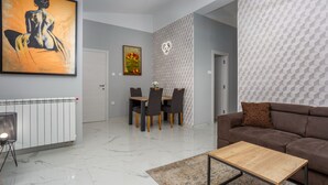 Una sala moderna con un sofá marrón, una mesa de centro de madera, una zona de comedor con mesa y sillas, y un cuadro abstracto grande en la pared.