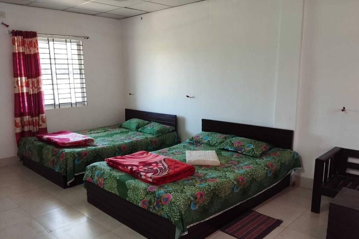 A room with two beds, each with a floral bedspread and pillows, a window with curtains, and a tiled floor.