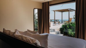 Ein Hotelzimmer mit Bett, Blick auf den Strand und einer Terrasse mit Gartenmöbeln.