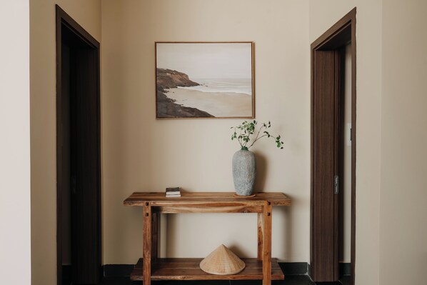 A hallway with a wooden console table, a vase with green plants, and a framed picture of a beach. - A STAY IN CICI (Hue)