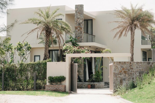 Una casa moderna con fachada de piedra, palmeras y entrada protegida por una reja.