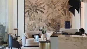 A modern lobby with a large botanical mural, a reception desk, a sofa, a striped armchair, and a coffee table with books. - Condor Concept 7 - JVC Holiday Homes (Dubai)