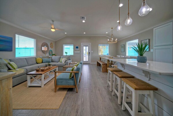 A spacious living room with a sofa, coffee table, and chairs, a kitchen area with a long counter and stools, and a dining area with a bench.