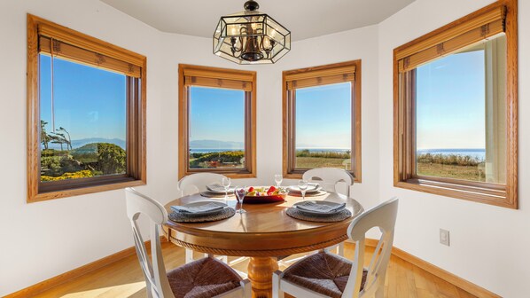 Comedor con una mesa redonda, cuatro sillas y vista al paisaje a través de amplios ventanales.