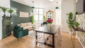 A modern living room with a green sofa, a dining table with clear chairs, and a decorative mirror. - Family Suites - Martin III-IV (Paris)