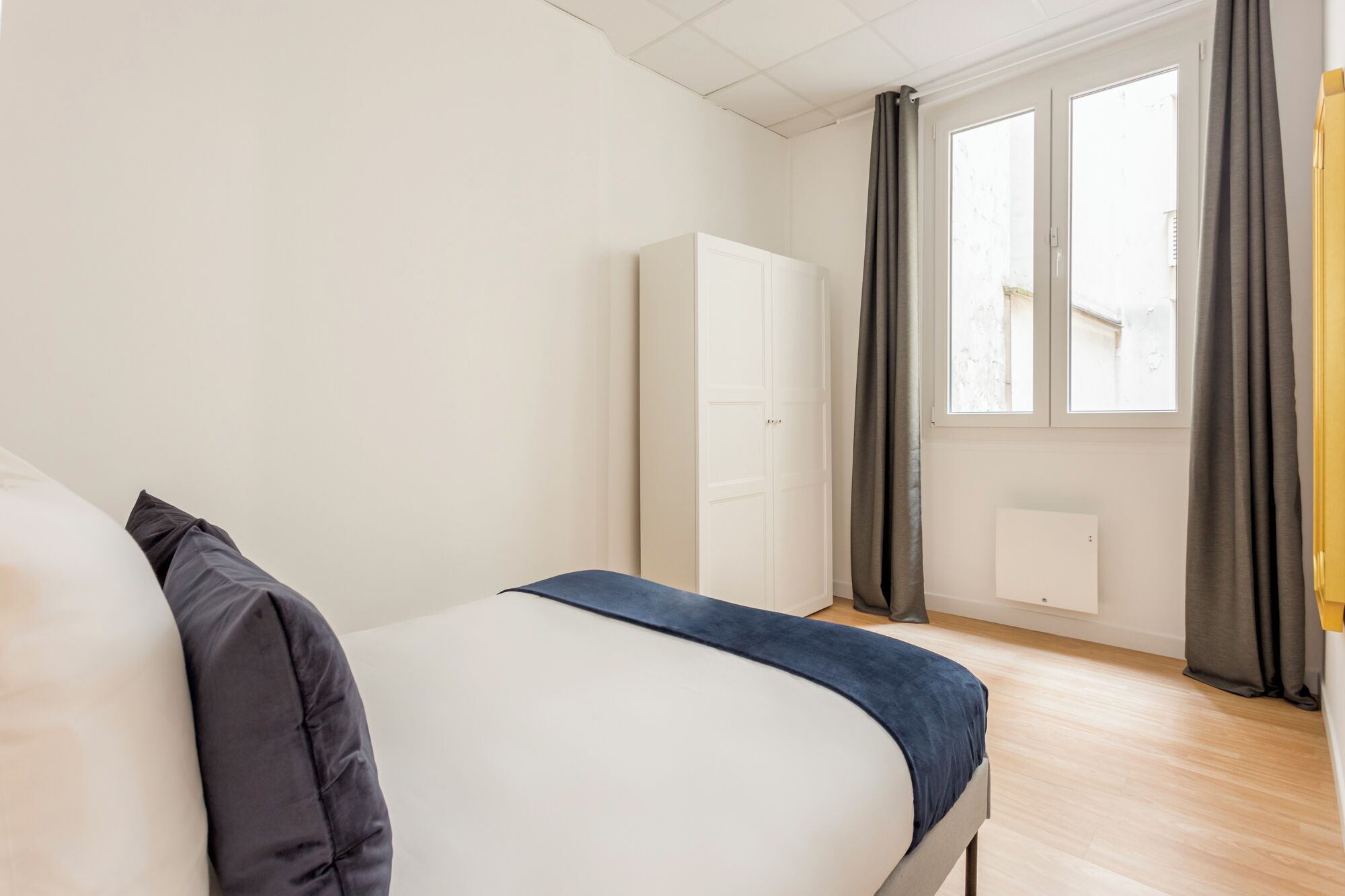 A bedroom with a bed, a wardrobe, and a window with curtains.