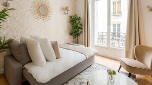 A modern living room with a grey sofa, a round mirror, and a large window with a view of a balcony. - Family Suites - Martin III-IV (Paris)