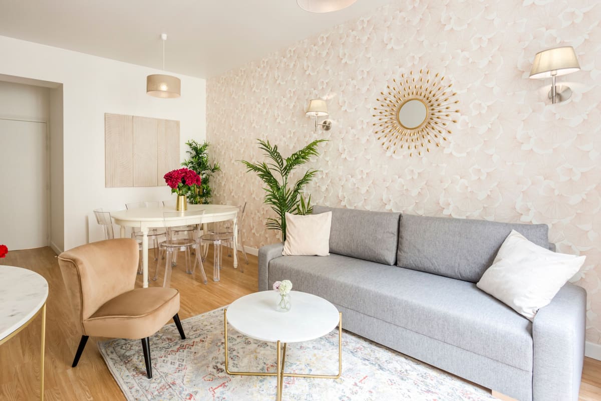 Uma sala de estar moderna com um sofá cinzento, uma mesa de centro redonda e um espaço de jantar com uma mesa e cadeiras brancas.