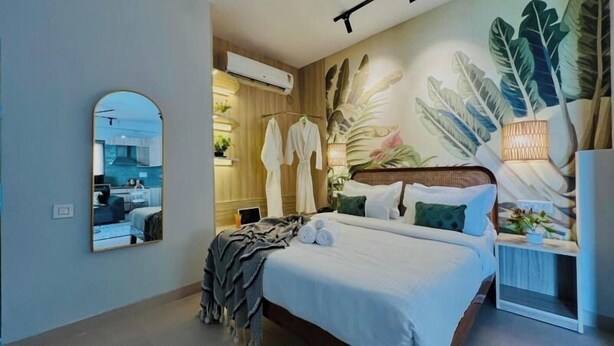 Ein Hotelzimmer mit einem Bett, einem Spiegel, einer Wandklimaanlage und einem großen Wandbild mit tropischen Blättern.