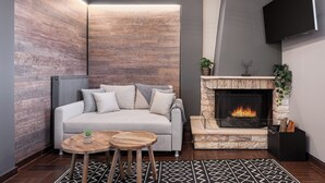 A modern living room with a fireplace, a sofa, and a TV mounted on the wall. - Tilemachos by GM Luxury Suites Kalavryta (Καλαβρύτa)