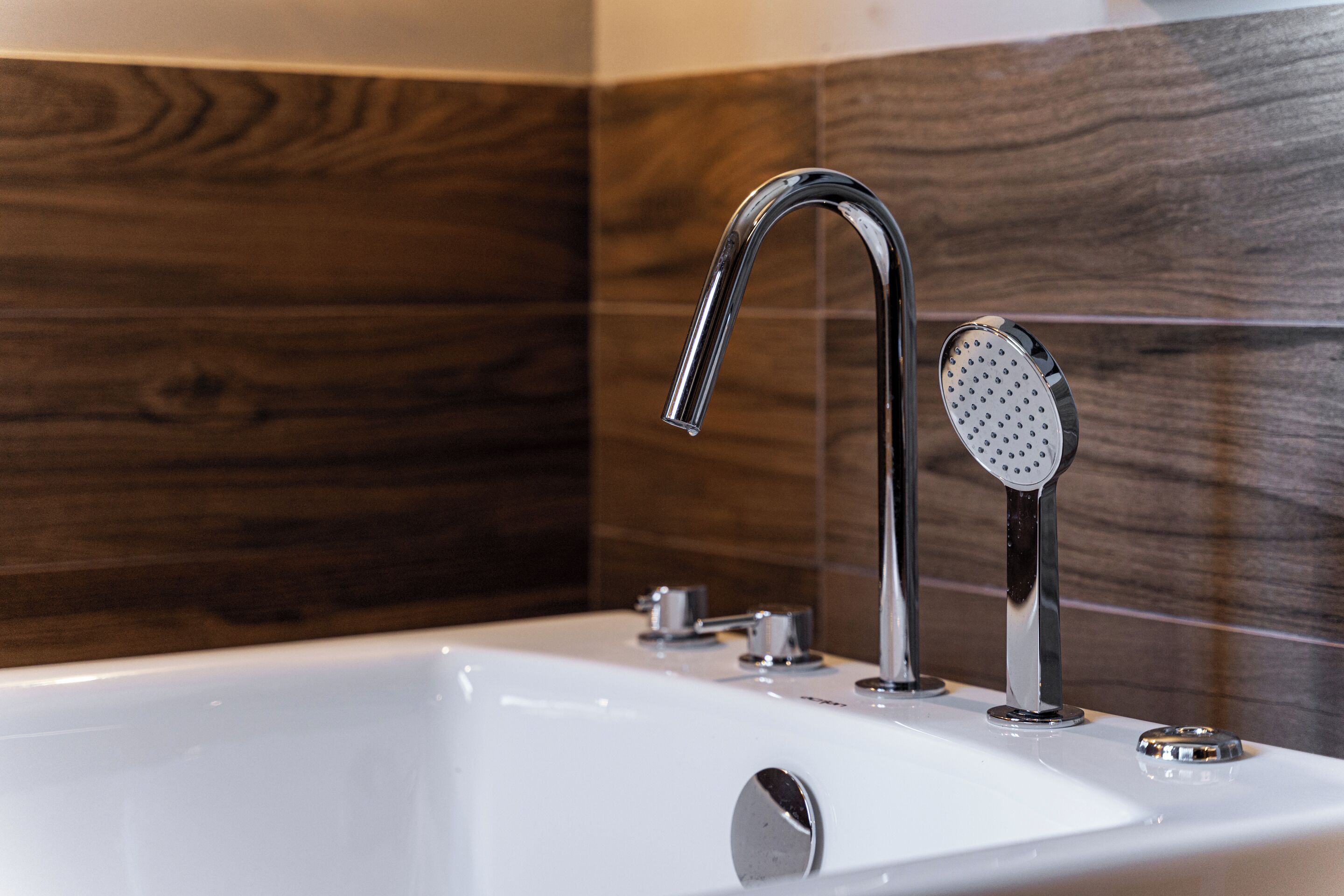 Een moderne badkamer met een wit bad, chroombeslag en houten wandtegels.