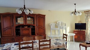 A dining area with a wooden table, chairs, a coffee maker, and a television on a stand. - Quiet house close to the sea and shops (Pornic)