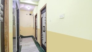A narrow hallway with a tiled floor, a door on the right, and a light switch on the wall. - Hotel New Om Shanti International (Kolkata)