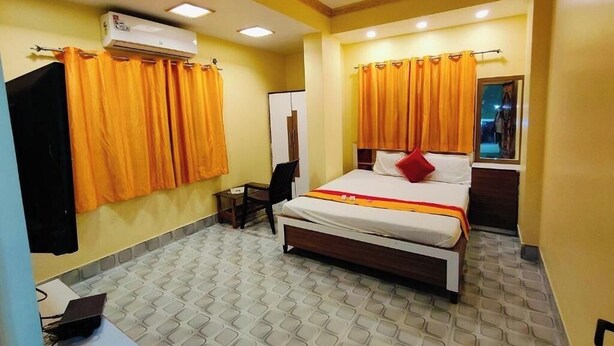 A hotel room with a bed, a desk, an air conditioner, and curtains. - Hotel New Om Shanti International (Kolkata)