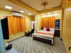 A hotel room with a bed, a desk, an air conditioner, and curtains.