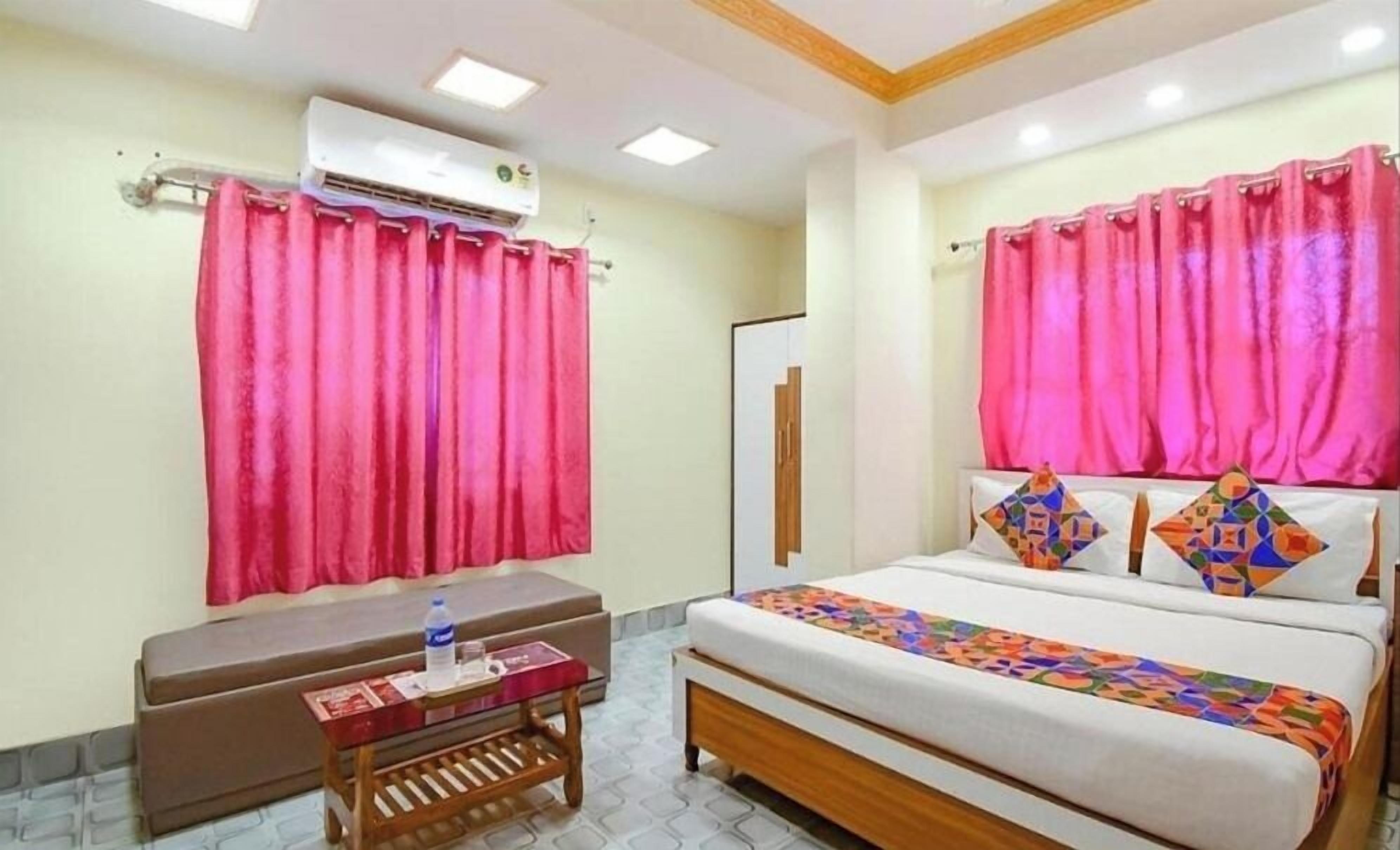 Una camera d'albergo con un letto, un comodino con una bottiglia d'acqua e tende rosa.