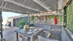 An outdoor patio with wicker furniture, a table set for dining, and a decorative wall with plants and flowers. - Studio in Denia with private pool (Denia)