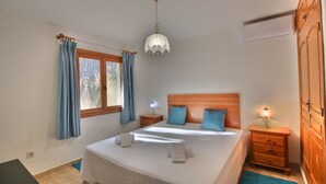 A neatly arranged bedroom with a bed, two pillows, a nightstand with a lamp, a wooden wardrobe, and a window with curtains. - Studio in Denia with private pool (Denia)
