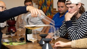 Een groep mensen bij een proefevenement met wijnglazen en een fles op een houten tafel.