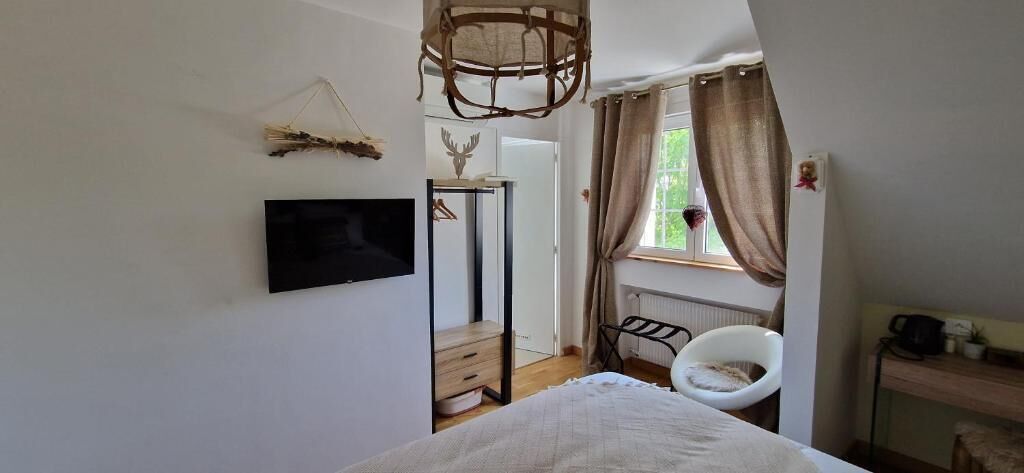 A bedroom with a bed, a mirror, a dresser, a chair, a radiator, and a window with curtains.